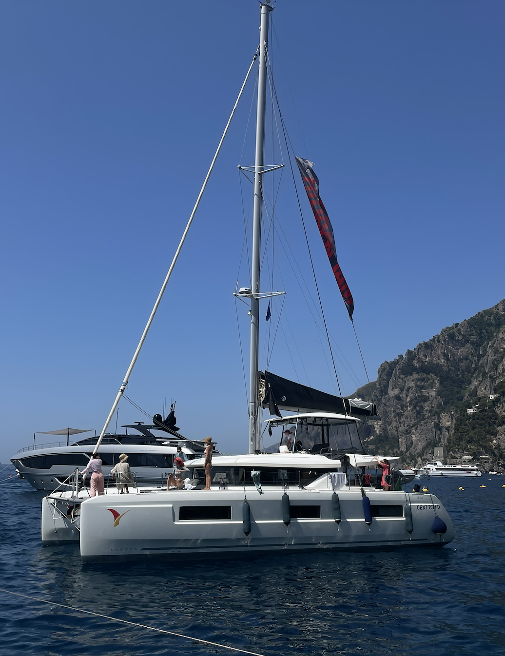 Crew on the deck of a white catamaran moored in deep blue water below rocky mountains