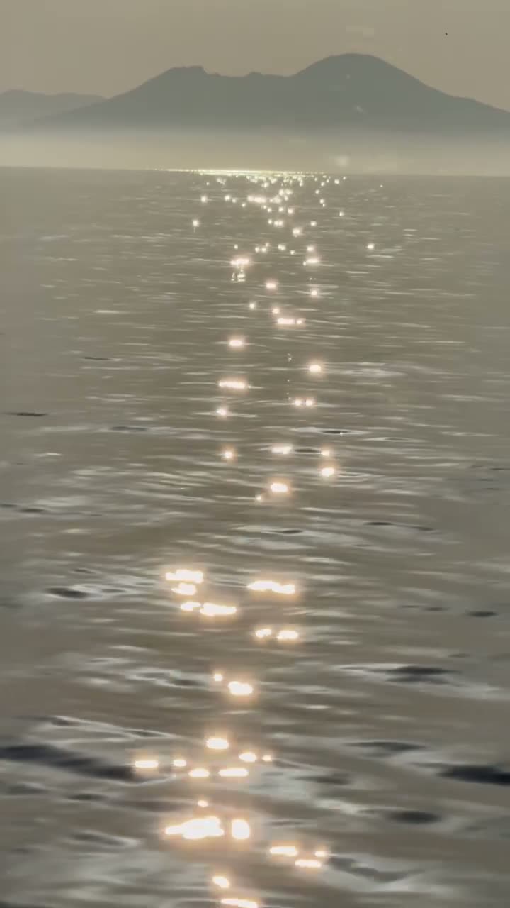 Sunlight glittering on calm water below a hazy mountain horizon
