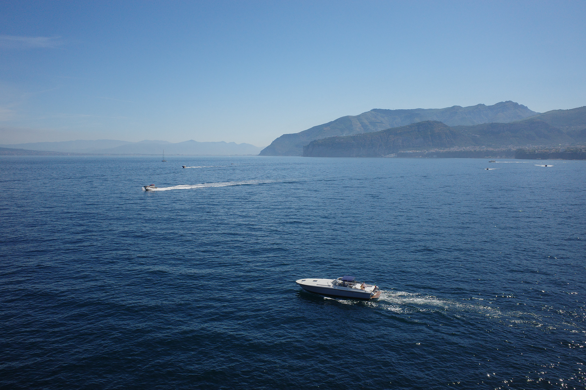 Motorboat crossing open blue water below a mountainous coast